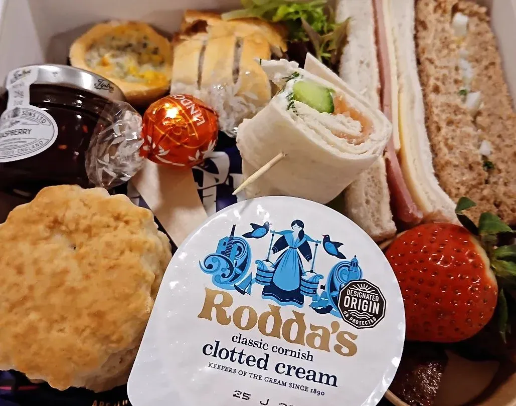 An afternoon tea box with sandwiches, scones, sausage roll and brownie